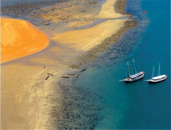 Vista aérea do Parque Marinho da Coroa Alta, em Santa Cruz Cabrália, na Bahia, com bancos de areia, águas cristalinas e barcos de passeio ancorados no local.