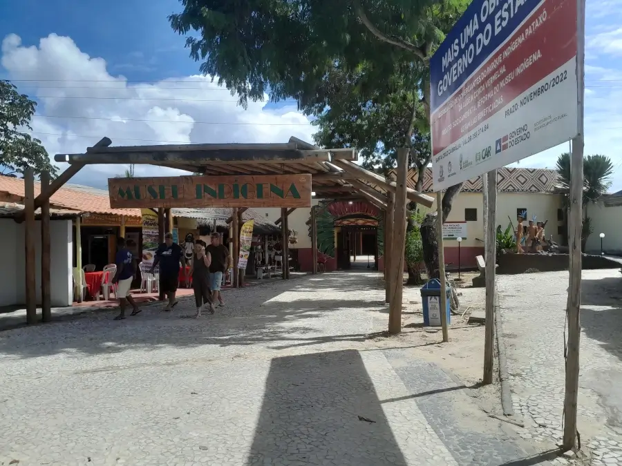 Entrada do Museu Indígena da Coroa Vermelha, em Santa Cruz Cabrália, na Bahia, com visitantes caminhando e placas indicativas sobre o espaço cultural Pataxó.