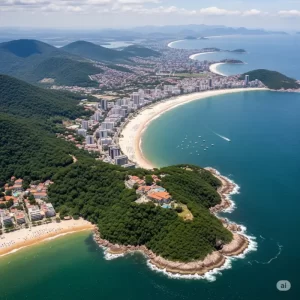 Vista aérea da cidade de Ubatuba, no Litoral Norte de SP, mostrando a praia, o mar azul e as montanhas da Serra do Mar.