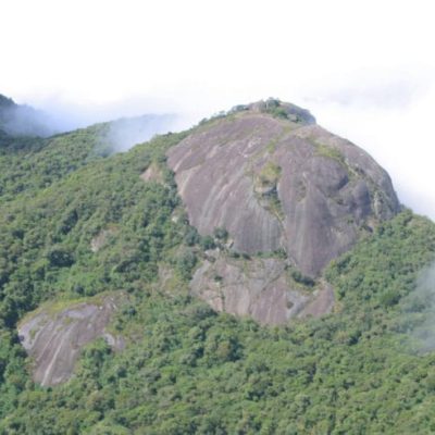 Vista do Chapéu do Bispo, formação rochosa característica de Monte Verde, Minas Gerais, cercado pela densa vegetação da Serra da Mantiqueira e com névoa entre as montanhas.