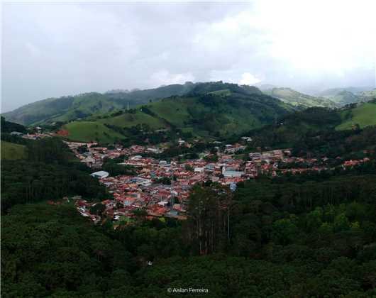 Paisagem rural com montanhas verdejantes sob um céu com nuvens dramáticas em Gonçalves, representando a tranquilidade e a beleza natural da região.