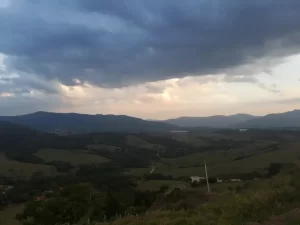 Ampla vista panorâmica das montanhas verdejantes e dos vales de Extrema, Minas Gerais, sob um céu com nuvens carregadas, transmitindo a tranquilidade da região.