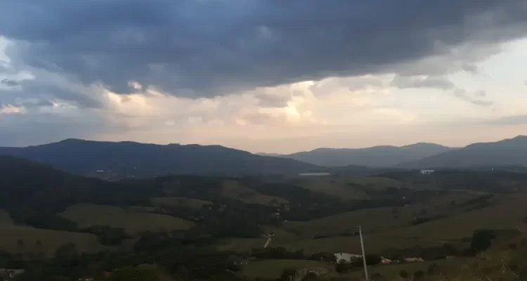 Ampla vista panorâmica das montanhas verdejantes e dos vales de Extrema, Minas Gerais, sob um céu com nuvens carregadas, transmitindo a tranquilidade da região.