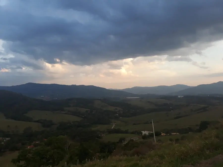 Ampla vista panorâmica das montanhas verdejantes e dos vales de Extrema, Minas Gerais, sob um céu com nuvens carregadas, transmitindo a tranquilidade da região.