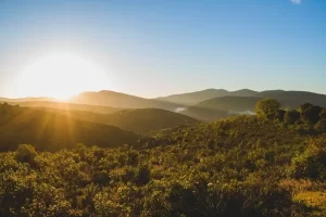 Paisagem com montanhas verdes e o nascer do sol ao fundo, representando a região da Serra da Mantiqueira em Minas Gerais.