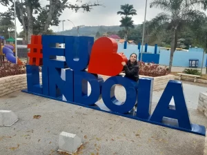 Marcia Lira, redatora do blog Viagens e Passeios, posando para foto no letreiro turístico colorido "#EuAmoLindoia", localizado em uma praça da cidade. Foto arquivo pessoal.