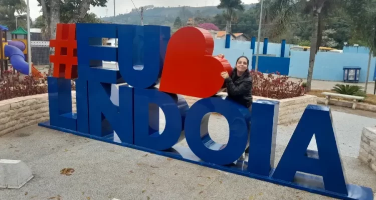 Marcia Lira, redatora do blog Viagens e Passeios, posando para foto no letreiro turístico colorido "#EuAmoLindoia", localizado em uma praça da cidade. Foto arquivo pessoal.