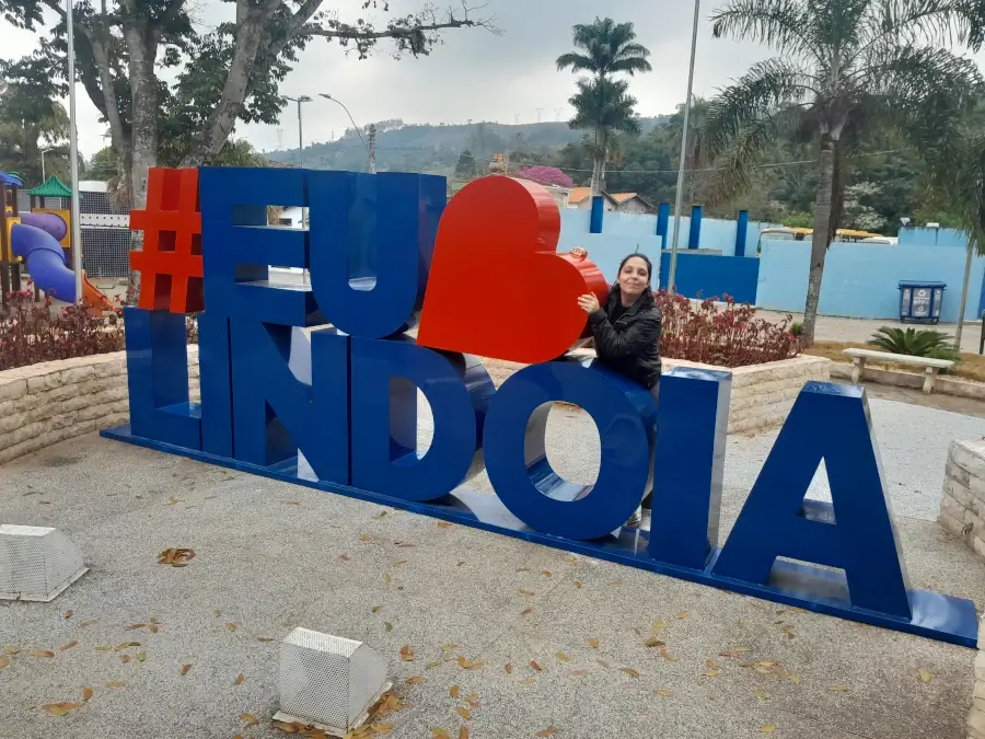 Marcia Lira, redatora do blog Viagens e Passeios, posando para foto no letreiro turístico colorido "#EuAmoLindoia", localizado em uma praça da cidade. Foto arquivo pessoal.