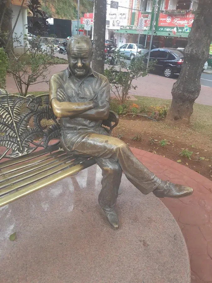 Estátua de bronze do humorista Ronald Golias sentado em um banco de praça, localizada na Praça John Fitzgerald em Serra Negra.