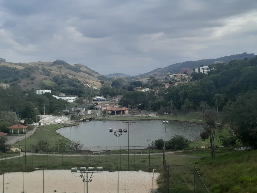 Vista do "Laguinho" de Lindóia, com suas águas calmas, cercado por vegetação e com a cidade e morros ao fundo em um dia nublado.