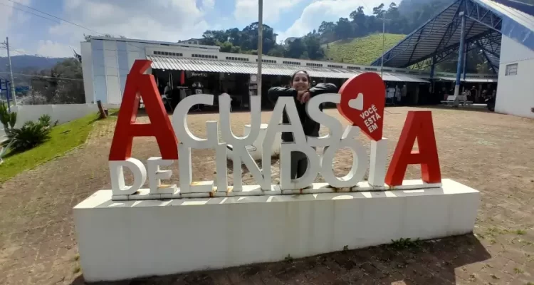 Marcia Lira, redatora do blog Viagens e Passeios, posando para foto atrás do letreiro de Águas de Lindóia, que está na Praça do Artesão. Ela está sorrindo com os braços apoiados no letreiro. Foto: arquivo pessoal.