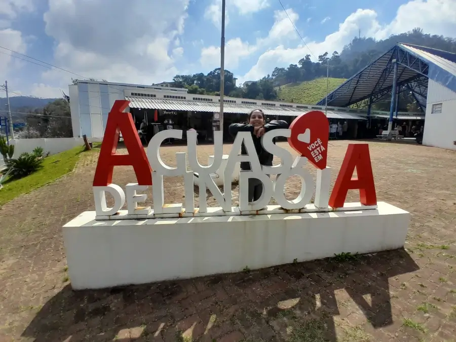 Marcia Lira, redatora do blog Viagens e Passeios, posando para foto atrás do letreiro de Águas de Lindóia, que está na Praça do Artesão. Ela está sorrindo com os braços apoiados no letreiro. Foto: arquivo pessoal.