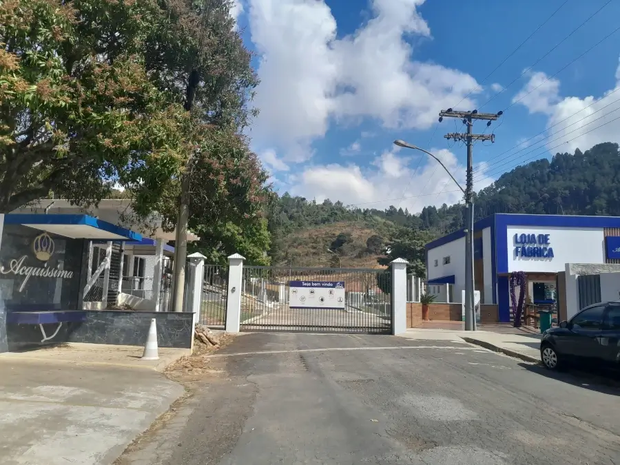 Fachada da Loja de Fábrica da Aquíssima, com portões brancos e um prédio azul ao lado, em Águas de Lindóia.