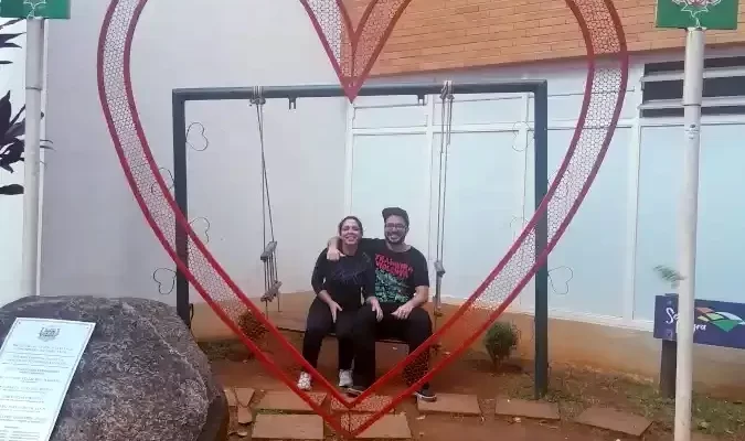 Casal do Viagens e Passeios, sentado, posando para fotografia em arco da cidade Serra Negra.