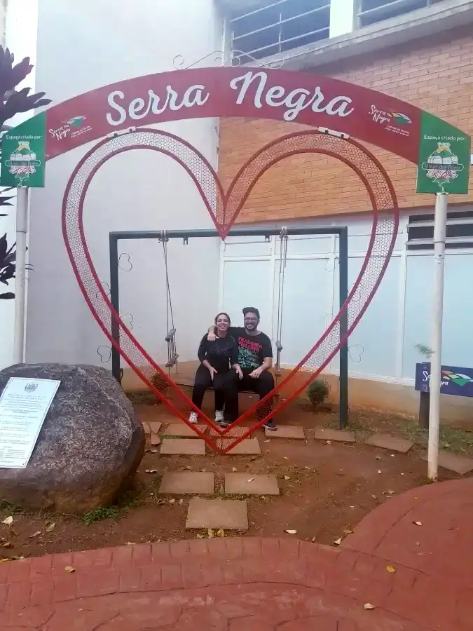 Casal do Viagens e Passeios, sentado, posando para fotografia em arco da cidade Serra Negra.