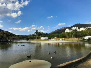 Vista panorâmica do lago da Praça Adhemar de Barros em Águas de Lindóia, com gansos na água e a paisagem verde do Circuito das Águas Paulista ao fundo. Foto: arquivo pessoal.