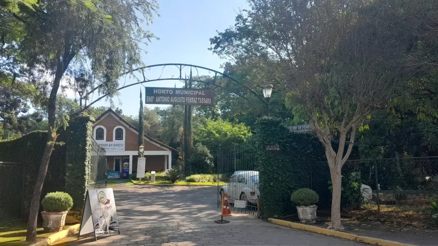 Portão de entrada do Horto Municipal de Socorro, com um arco de metal e cercas vivas em um dia de sol.