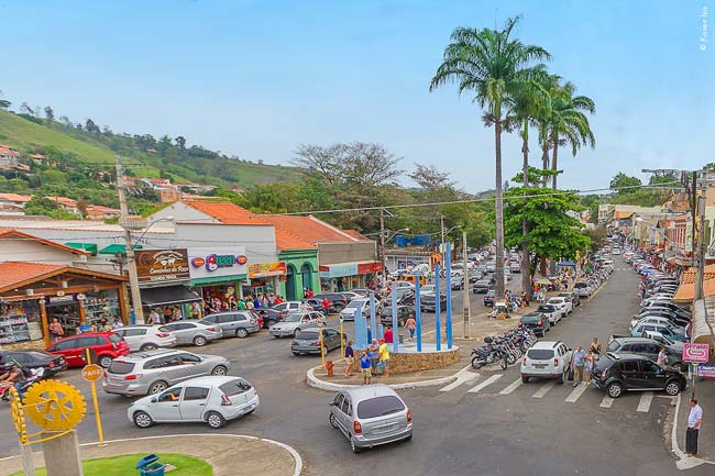 Rua comercial movimentada no centro de Pedreira, com diversas lojas de porcelana e decoração e carros estacionados.