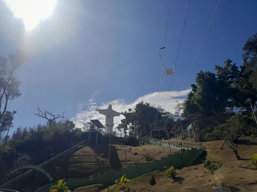 Vista do Cristo Redentor de Serra Negra e do teleférico subindo a montanha em um dia de sol forte.