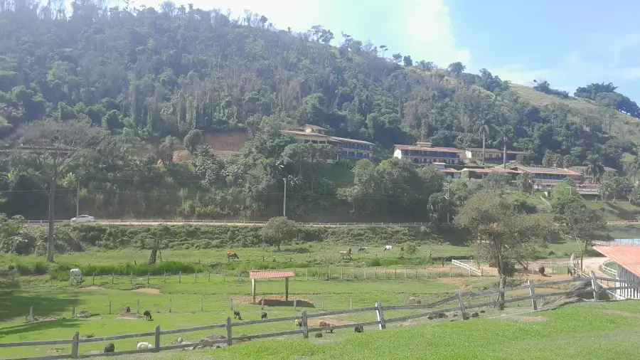 Vista panorâmica de um hotel fazenda em Socorro, com as construções na encosta de uma montanha verde e animais pastando no campo.