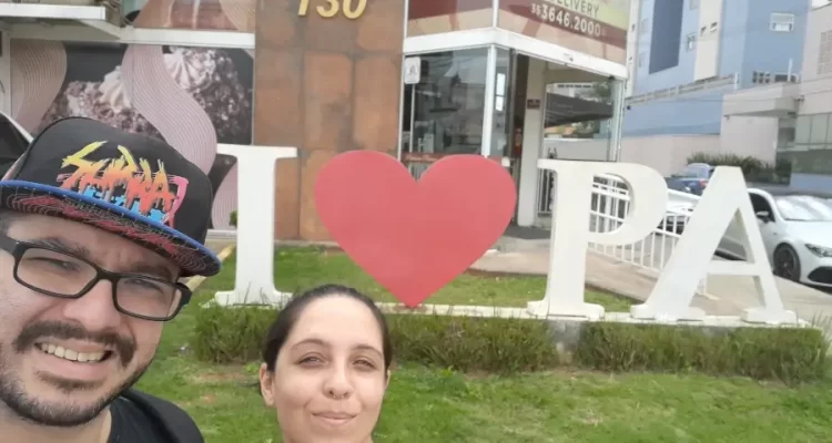 Casal de viajantes fundadores do Viagens e Passeios, Marcia Lira e Windsor Fernandes, tirando uma selfie sorrindo em frente ao letreiro turístico com um coração vermelho e as letras PA.