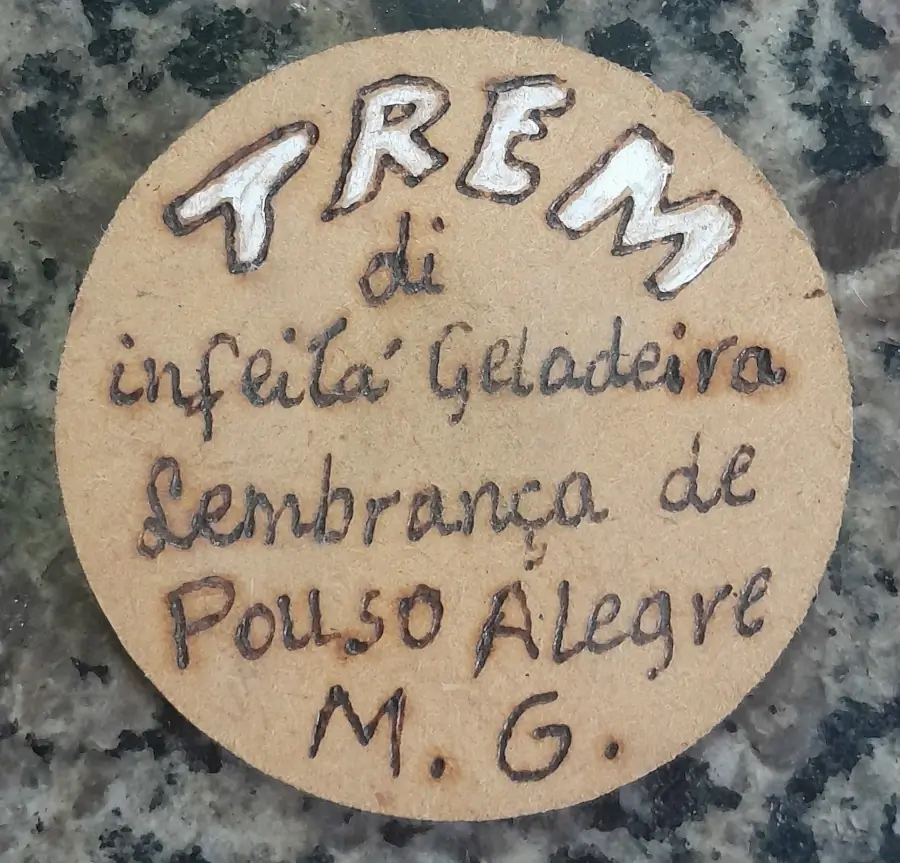Ímã de geladeira redondo feito de madeira com a frase mineira "Trem di infeitá geladeira" escrita à mão.