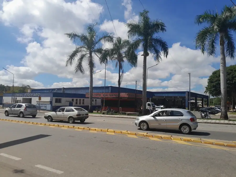 Fachada externa do Terminal Rodoviário de Pouso Alegre, um prédio azul com coqueiros na frente e carros passando.