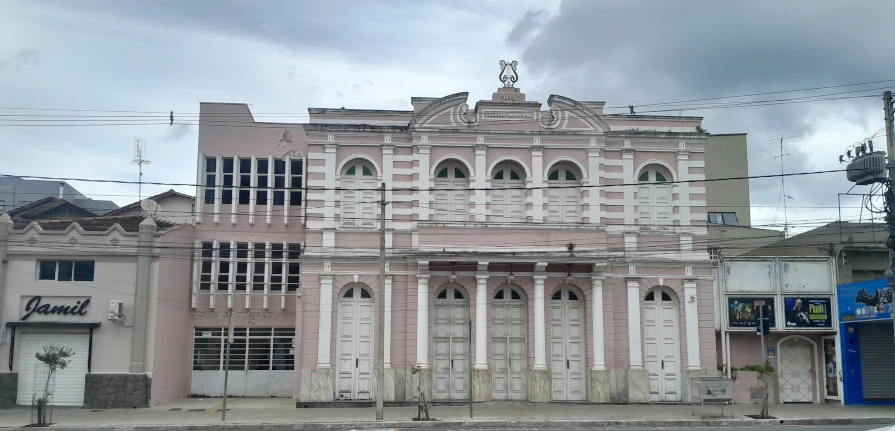 Fachada frontal do Teatro Municipal, um edifício histórico com arquitetura clássica pintado de rosa e detalhes brancos.